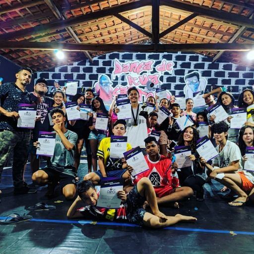 Grupo de jovens e adultos do projeto Dança de Rua Castelo a segurar os seus certificados de conclusão numa sala de estúdio, sorrindo para a câmara.